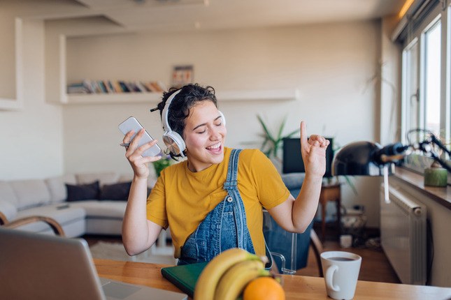 Photo d'une jeune femme à domicile, casque sur les oreilles, écoutant de la musique avec son téléphone