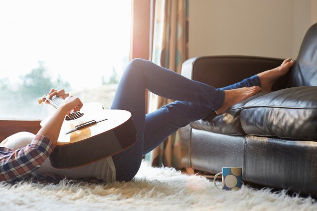 Photo d'une femme allongée avec sa guitare dans son salon